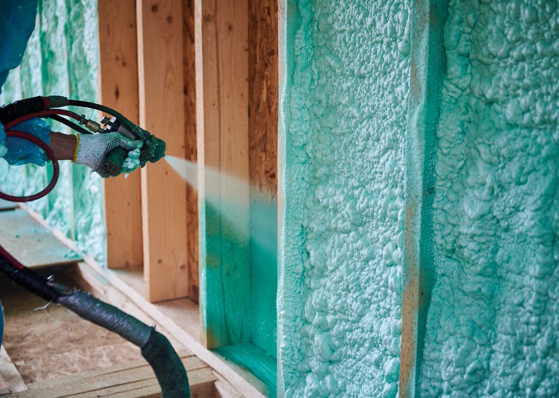 Worker spraying polyurethane foam for insulating wooden frame house.